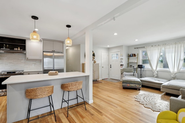 kitchen featuring stainless steel appliances, hanging light fixtures, a kitchen bar, and light wood-type flooring