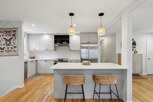 kitchen with a breakfast bar area, hanging light fixtures, appliances with stainless steel finishes, light hardwood / wood-style floors, and decorative backsplash