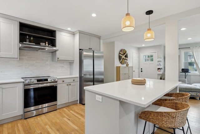 kitchen featuring a breakfast bar area, hanging light fixtures, light hardwood / wood-style flooring, stainless steel appliances, and decorative backsplash