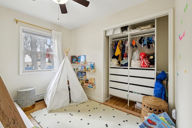 bedroom featuring ceiling fan, a baseboard radiator, hardwood / wood-style floors, and a closet