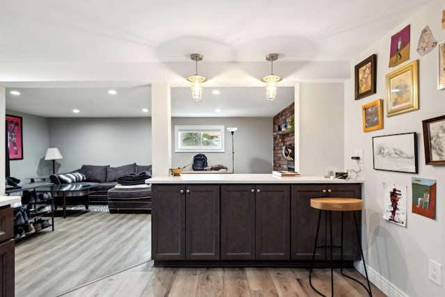 kitchen with pendant lighting, dark brown cabinets, light hardwood / wood-style floors, and kitchen peninsula