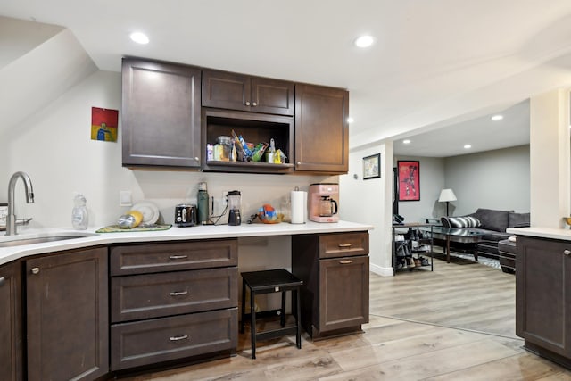 bar with sink, dark brown cabinetry, and light hardwood / wood-style floors