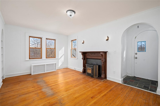 unfurnished living room with baseboards, visible vents, arched walkways, wood finished floors, and a wood stove