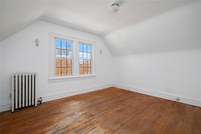 additional living space with vaulted ceiling, radiator, and dark wood finished floors