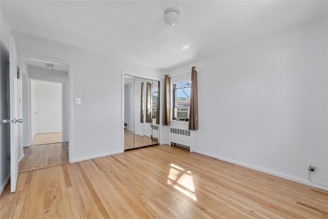 unfurnished bedroom with radiator, a closet, wood-type flooring, attic access, and baseboards