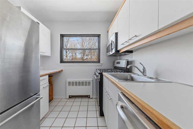 kitchen with appliances with stainless steel finishes, radiator, white cabinetry, and a sink