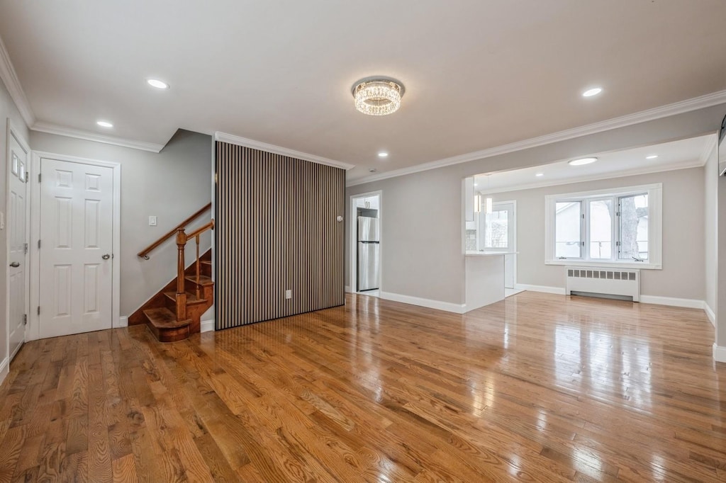 unfurnished living room with crown molding, radiator heating unit, and light hardwood / wood-style floors