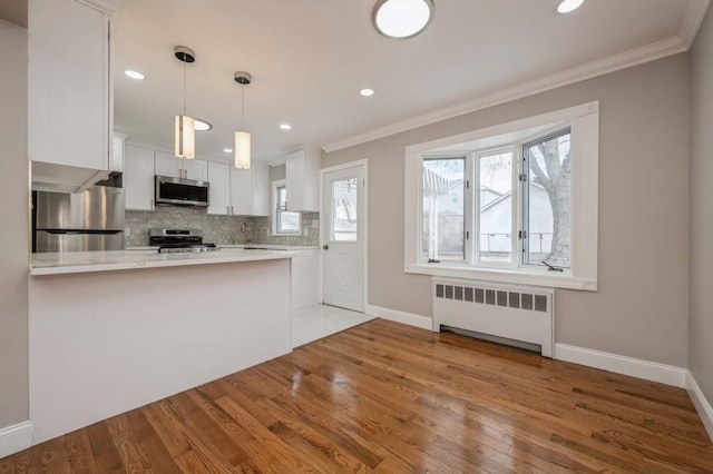 kitchen featuring white cabinetry, tasteful backsplash, appliances with stainless steel finishes, radiator heating unit, and kitchen peninsula