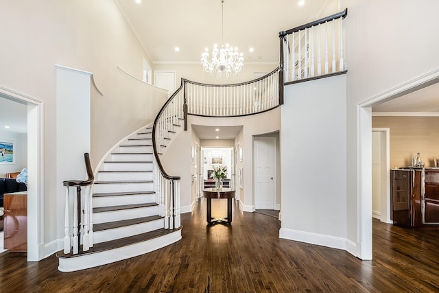 entryway with ornamental molding, dark wood-type flooring, an inviting chandelier, and a towering ceiling