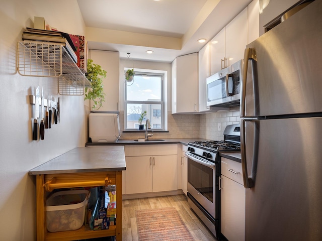 kitchen featuring sink, light wood-type flooring, stainless steel appliances, decorative backsplash, and white cabinets