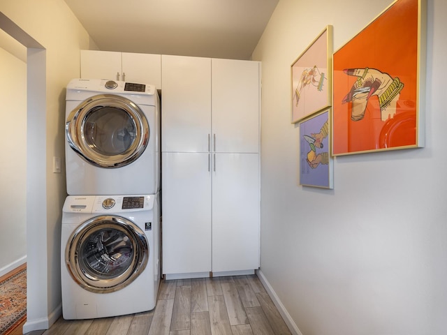 clothes washing area with cabinets, stacked washer / drying machine, and light hardwood / wood-style floors