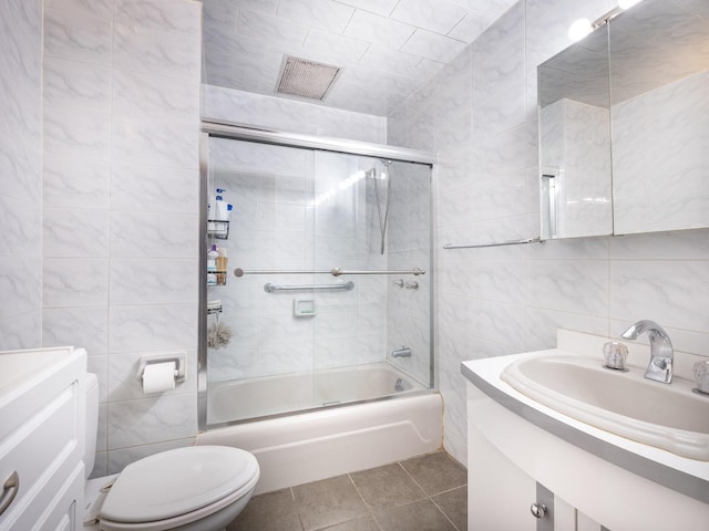 full bathroom featuring shower / bath combination with glass door, tile walls, tile patterned flooring, vanity, and toilet