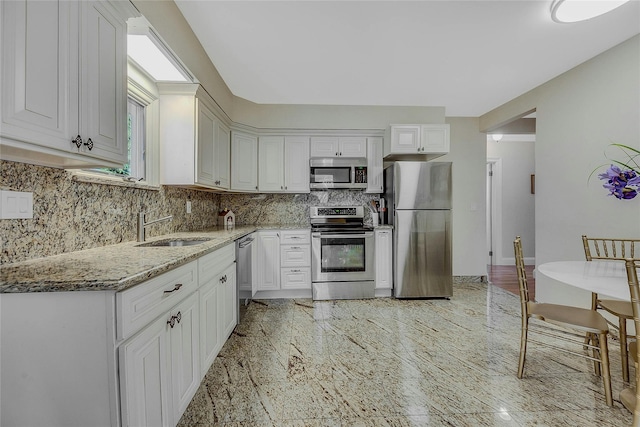 kitchen featuring sink, white cabinetry, stainless steel appliances, tasteful backsplash, and light stone countertops