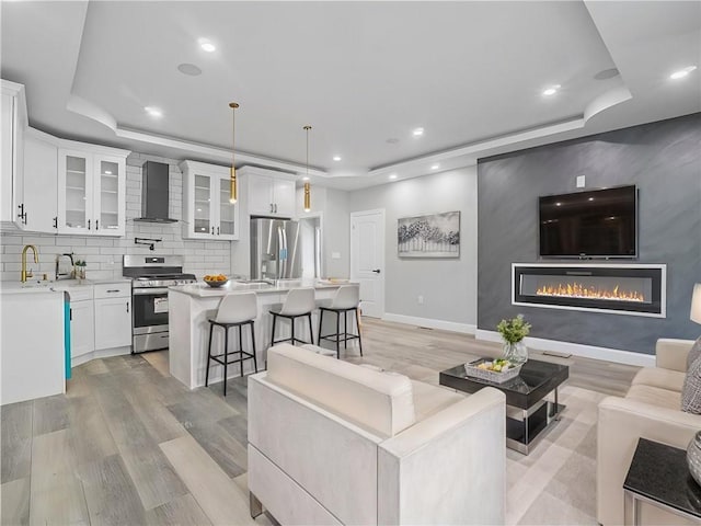 living room with sink, a tray ceiling, and light hardwood / wood-style floors