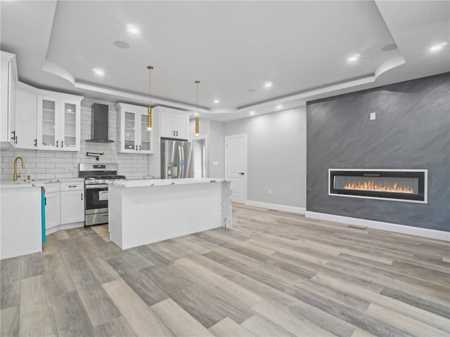 kitchen with wall chimney range hood, stainless steel appliances, a raised ceiling, and white cabinets