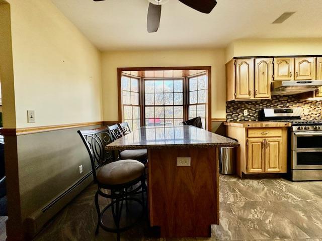 kitchen with tasteful backsplash, a baseboard radiator, a kitchen breakfast bar, ceiling fan, and range with two ovens