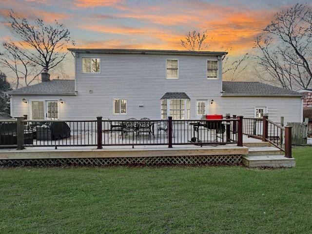 back house at dusk featuring a wooden deck and a lawn