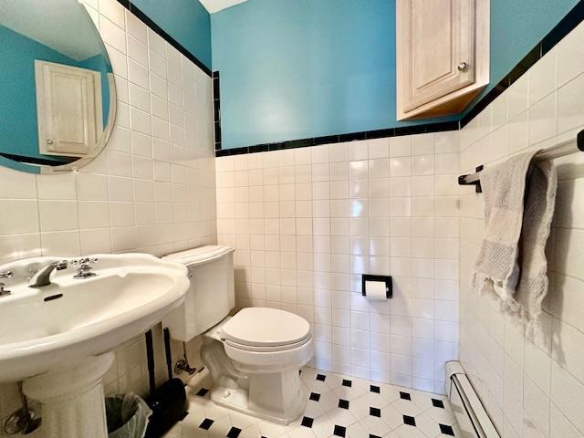 bathroom featuring baseboard heating, toilet, sink, and tile walls