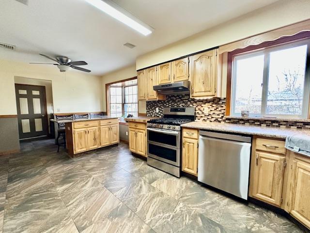 kitchen featuring light brown cabinetry, backsplash, ceiling fan, and appliances with stainless steel finishes