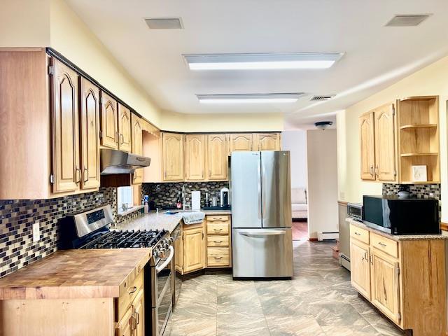 kitchen with wooden counters, baseboard heating, appliances with stainless steel finishes, tasteful backsplash, and light brown cabinetry