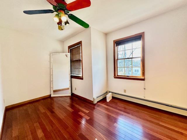 unfurnished bedroom with dark wood-type flooring, ceiling fan, and a baseboard heating unit