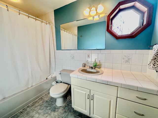 full bathroom with shower / bath combo, tile patterned flooring, tile walls, vanity, and toilet