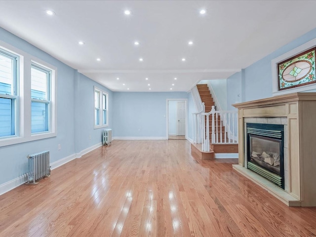 unfurnished living room featuring radiator, a tile fireplace, and light wood-type flooring