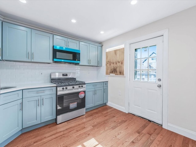 kitchen with sink, light hardwood / wood-style floors, decorative backsplash, and stainless steel gas range oven