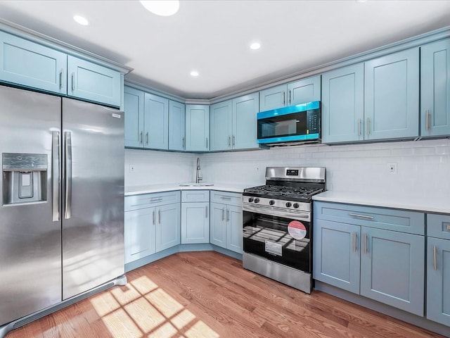 kitchen featuring tasteful backsplash, sink, light hardwood / wood-style floors, and appliances with stainless steel finishes