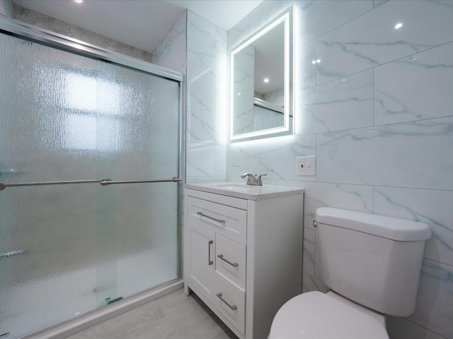 bathroom featuring a shower with door, vanity, tile walls, and toilet