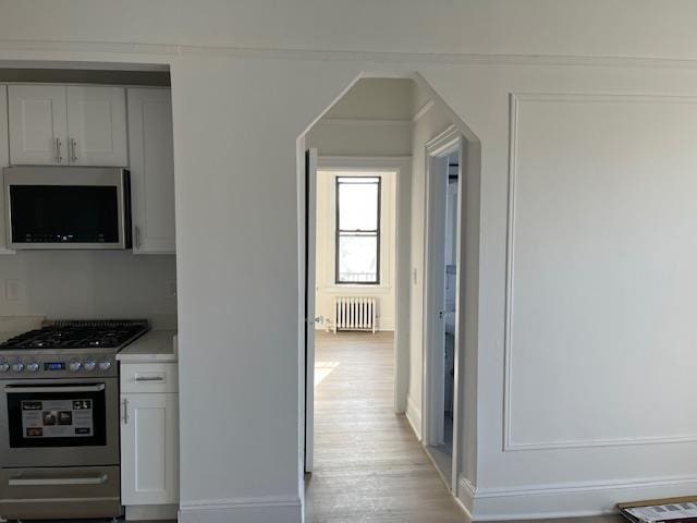 kitchen featuring white cabinetry, appliances with stainless steel finishes, radiator heating unit, and light hardwood / wood-style flooring