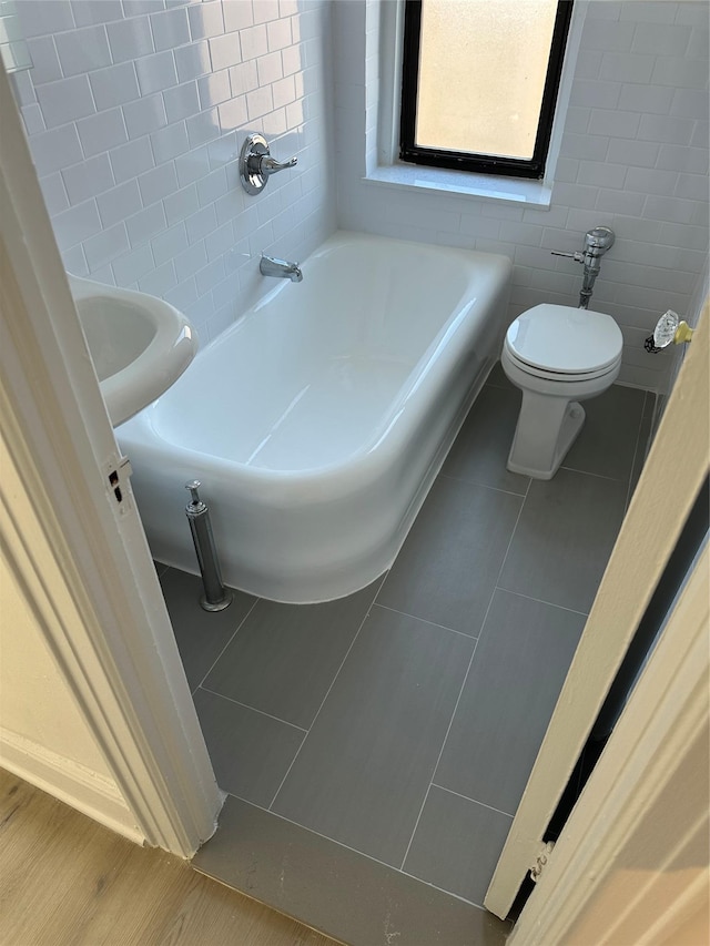 bathroom featuring toilet, tile patterned flooring, tile walls, and a washtub