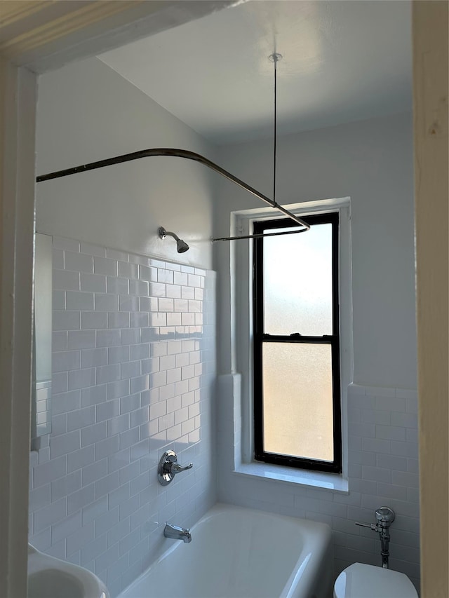 bathroom with toilet, tiled shower / bath combo, and tile walls