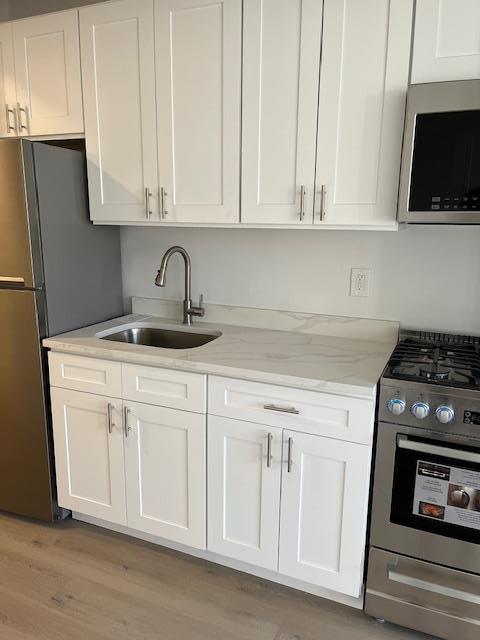 kitchen with sink, light hardwood / wood-style flooring, appliances with stainless steel finishes, light stone counters, and white cabinets