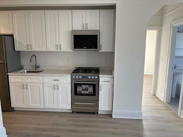 kitchen with sink, stainless steel appliances, white cabinets, and light wood-type flooring