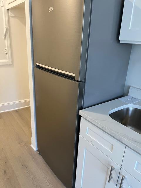 kitchen with stainless steel refrigerator, white cabinetry, sink, light stone counters, and light wood-type flooring