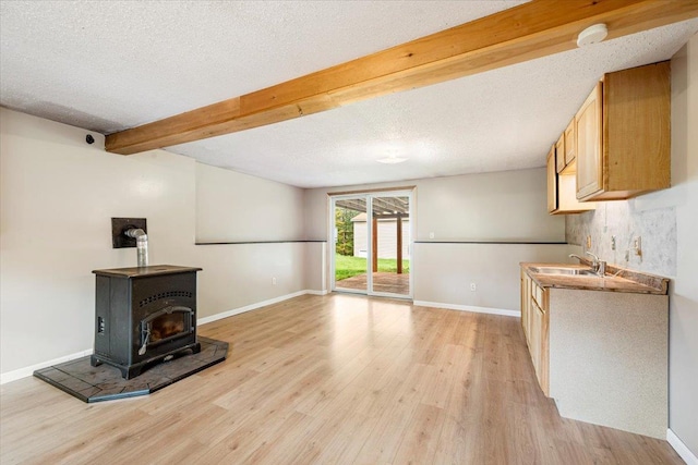 unfurnished living room featuring sink, a textured ceiling, light wood-type flooring, beamed ceiling, and a wood stove