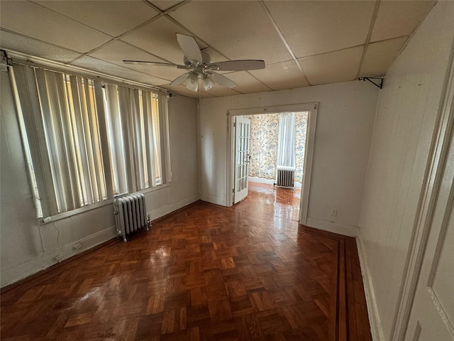 spare room with ceiling fan, radiator heating unit, dark parquet flooring, and a drop ceiling