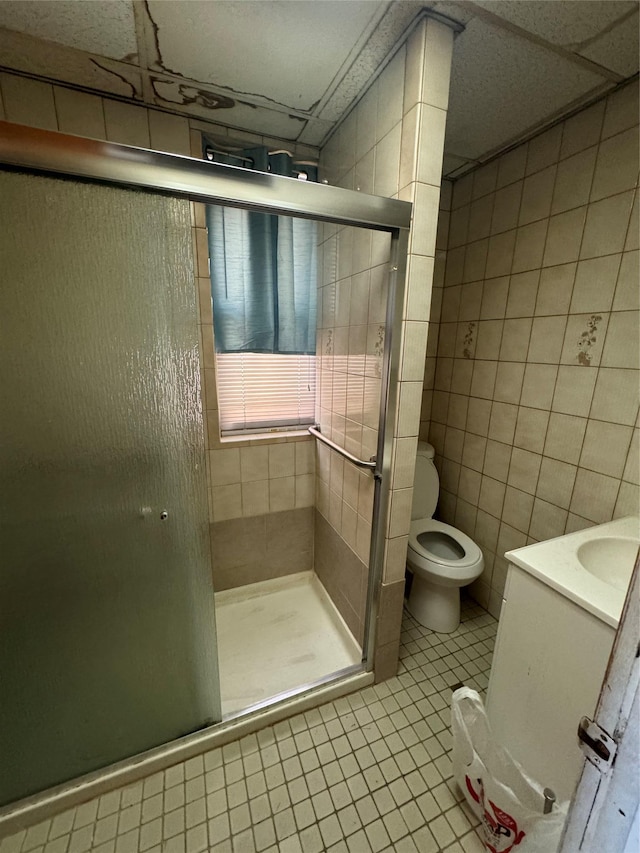 bathroom with toilet, an enclosed shower, tile walls, vanity, and tile patterned flooring