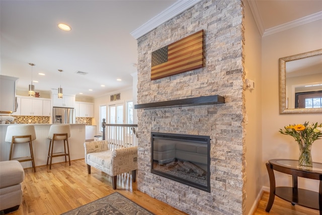 living room with visible vents, baseboards, a stone fireplace, light wood-style floors, and crown molding