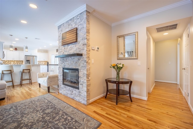 living room featuring crown molding, a fireplace, visible vents, and light wood finished floors