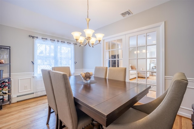 dining space with visible vents, a wainscoted wall, light wood-type flooring, baseboard heating, and an inviting chandelier