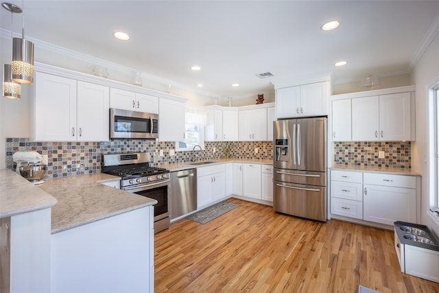 kitchen featuring a peninsula, a sink, ornamental molding, appliances with stainless steel finishes, and white cabinetry