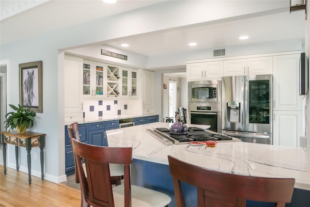 kitchen featuring blue cabinetry, light stone counters, stainless steel appliances, decorative backsplash, and white cabinets