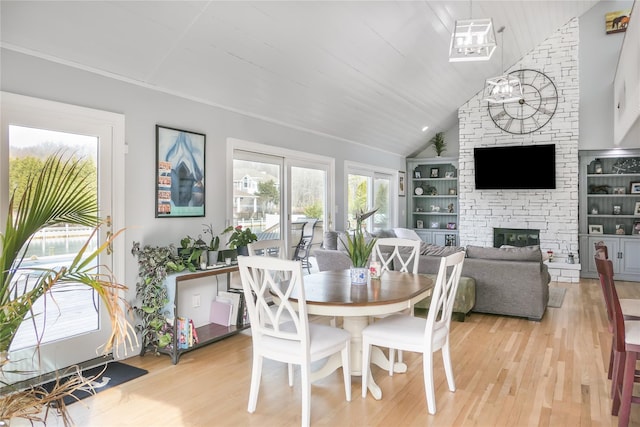 dining room with high vaulted ceiling, a stone fireplace, light hardwood / wood-style floors, and a chandelier