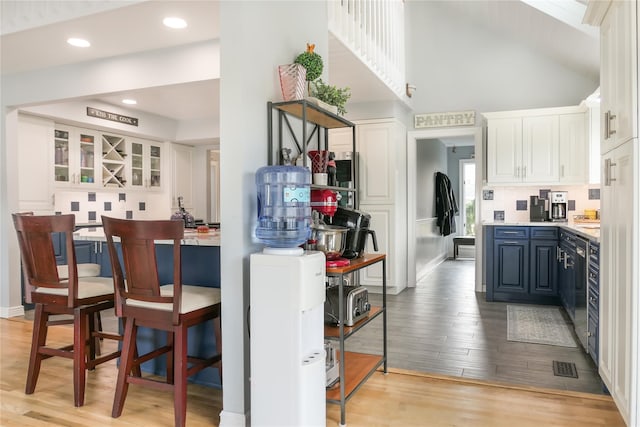 kitchen featuring high vaulted ceiling, blue cabinets, white cabinetry, dishwasher, and light hardwood / wood-style flooring