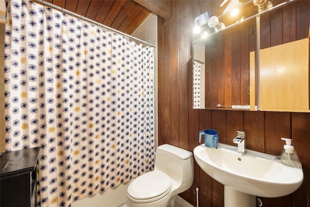 bathroom featuring sink, curtained shower, toilet, and wood walls