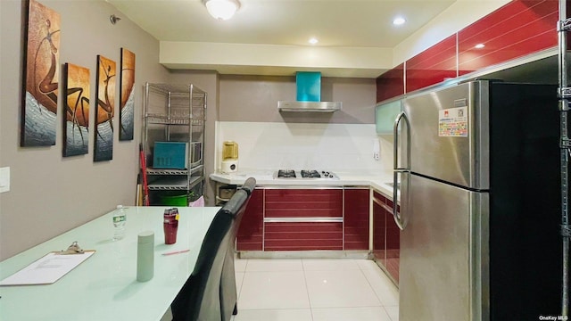 kitchen with white gas cooktop, light tile patterned floors, stainless steel refrigerator, decorative backsplash, and wall chimney range hood