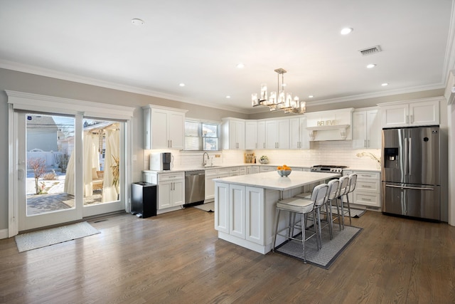 kitchen with appliances with stainless steel finishes, pendant lighting, white cabinets, dark hardwood / wood-style flooring, and a center island