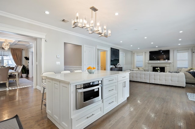 kitchen with white cabinetry, hanging light fixtures, a center island, light stone countertops, and an inviting chandelier